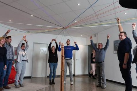 Group of employees standing in a circle around a stick with strings attached to it. 